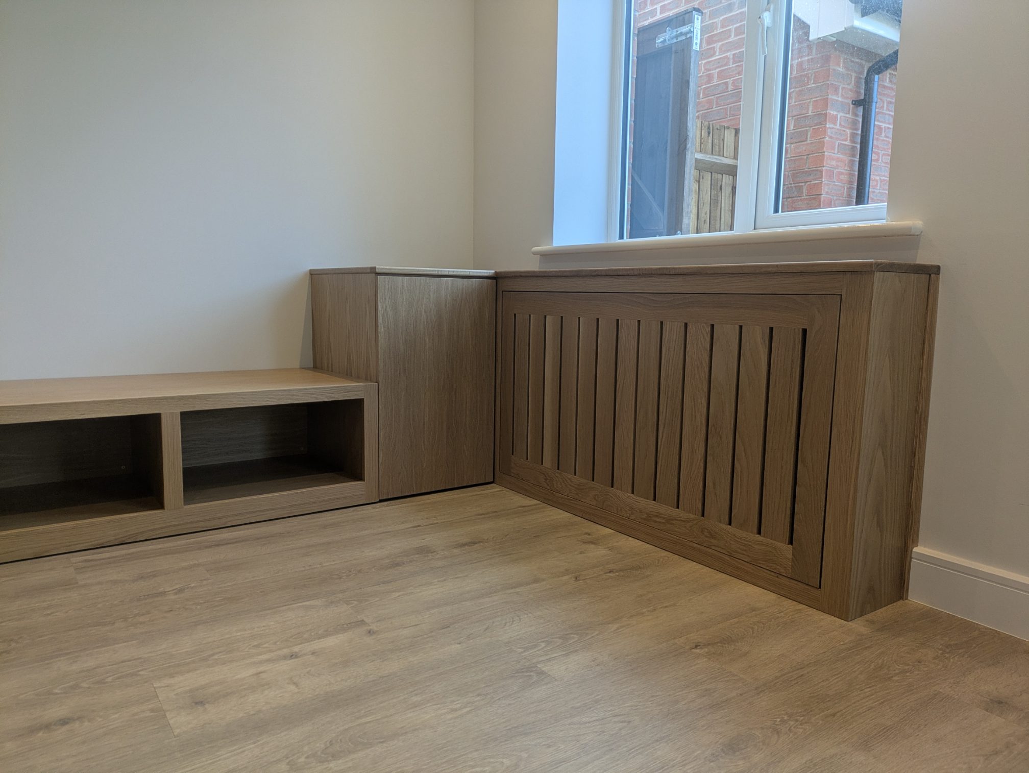 Oak radiator cover with a matching cupboard and open storage bench under a window